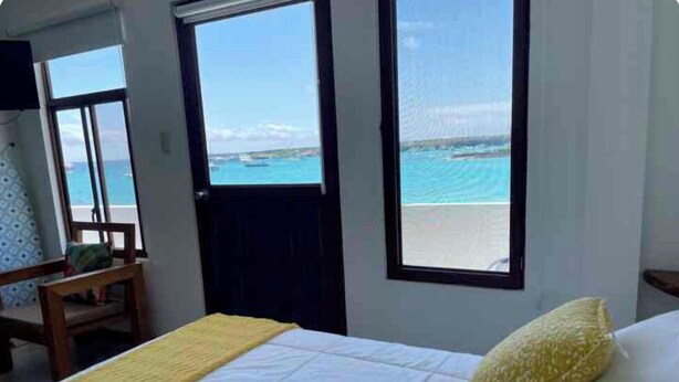 Un dormitorio con cama, una silla y vista al mar a través de amplios ventanales.