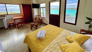 Habitación de hotel con cama, escritorio, silla y televisor. Amplias ventanas con vista al océano.