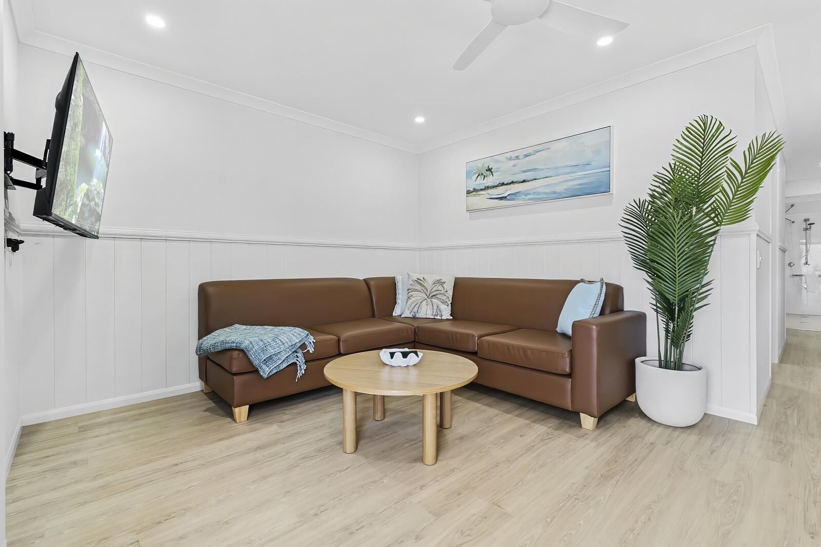 A modern living room with a brown leather sofa, a round wooden coffee table, and a large potted plant.