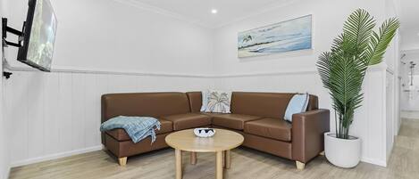 A modern living room with a brown leather sofa, a round wooden coffee table, and a large potted plant.