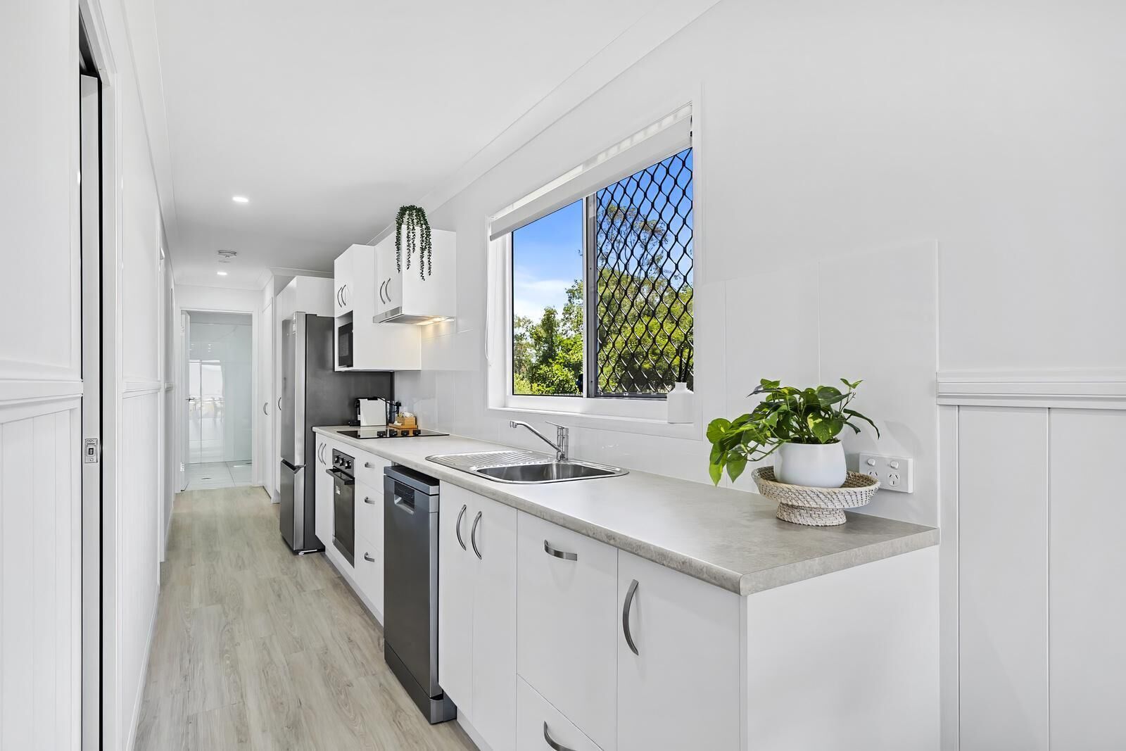 A modern kitchen with white cabinetry, a built-in dishwasher, and a window with a view of greenery.