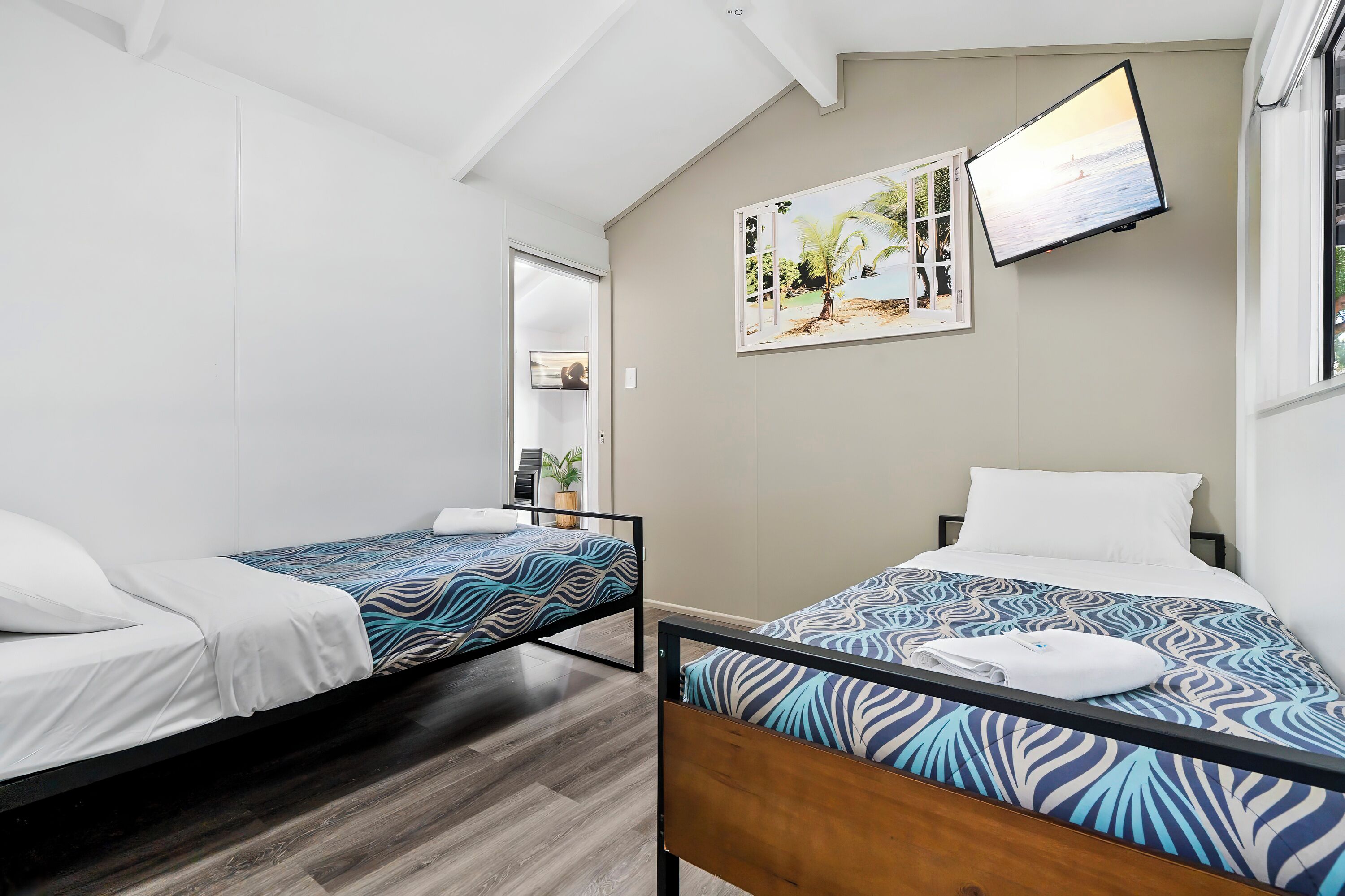 Een hotelkamer met twee eenpersoonsbedden, een flatscreen-tv aan de muur en een deur naar de badkamer.