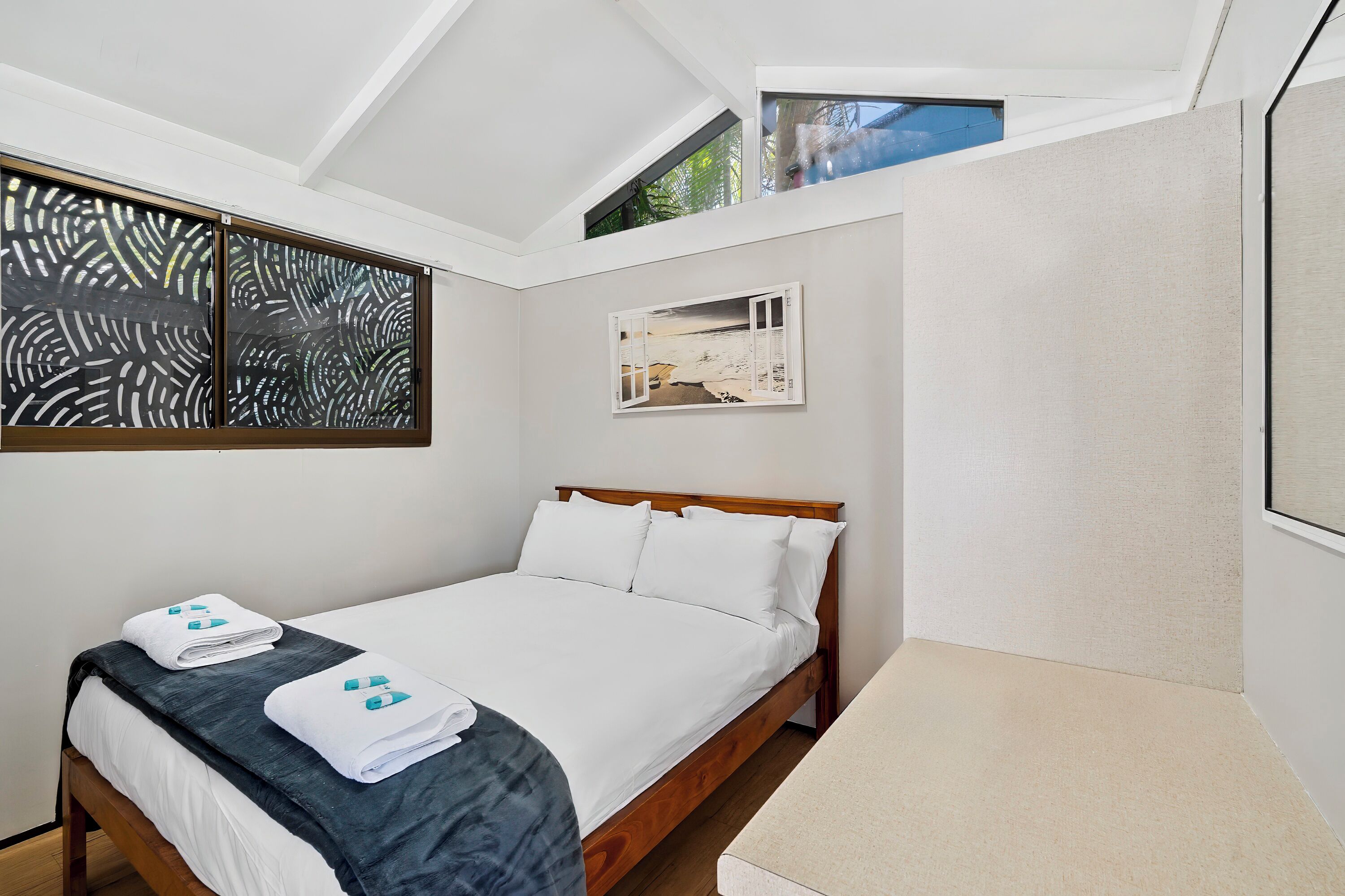 A bedroom with a bed, two towels, a window, and a painting.