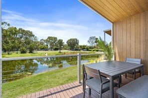 Terraza con mesa y sillas con vista a un estanque y un parque.