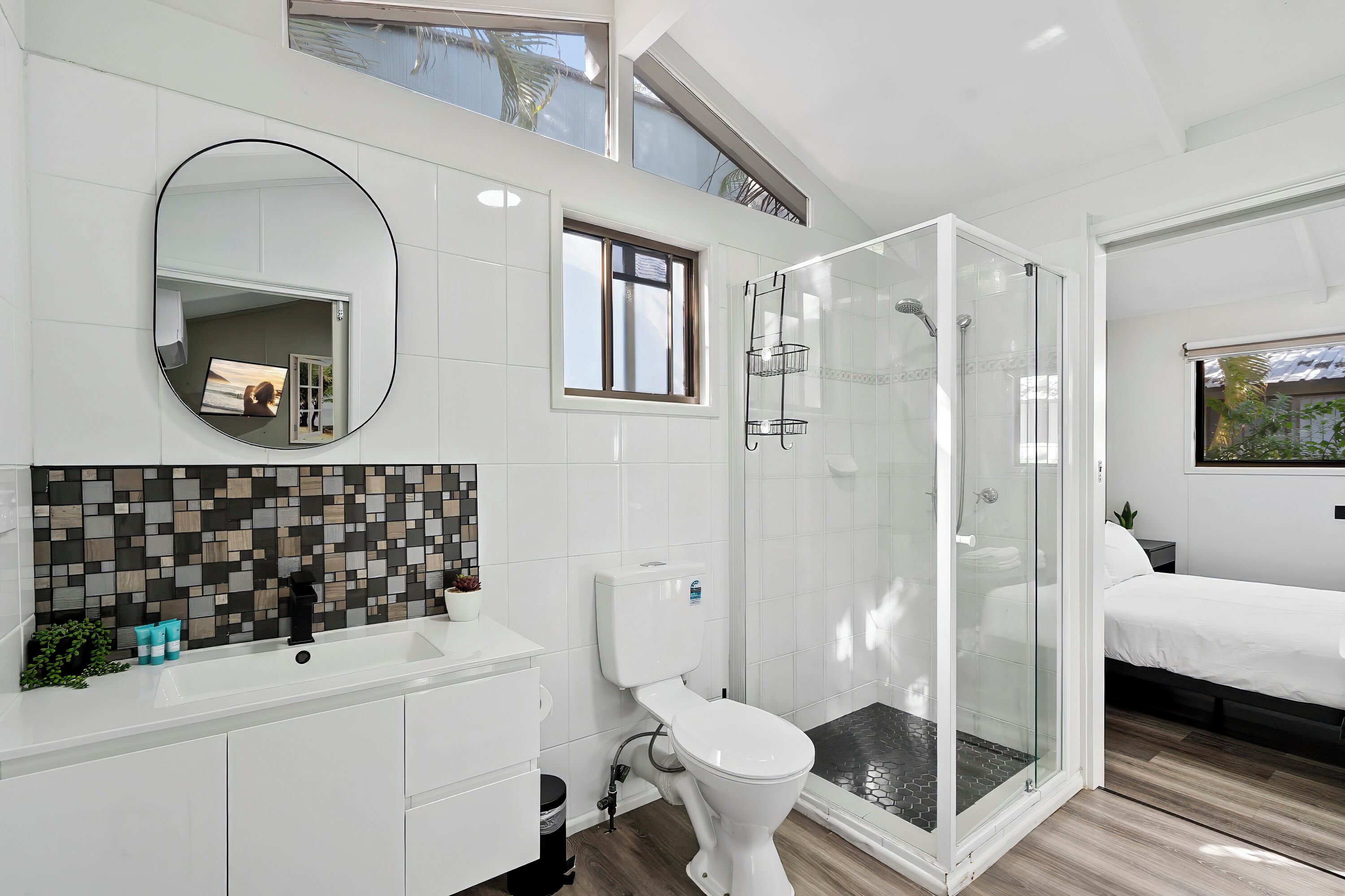 Un baño moderno con ducha envuelta en vidrio, inodoro blanco y lavamanos con resalte de azulejos.