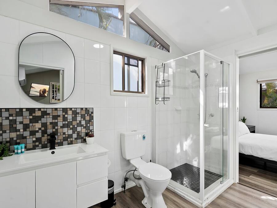 Un baño moderno con ducha envuelta en vidrio, inodoro blanco y lavamanos con resalte de azulejos.