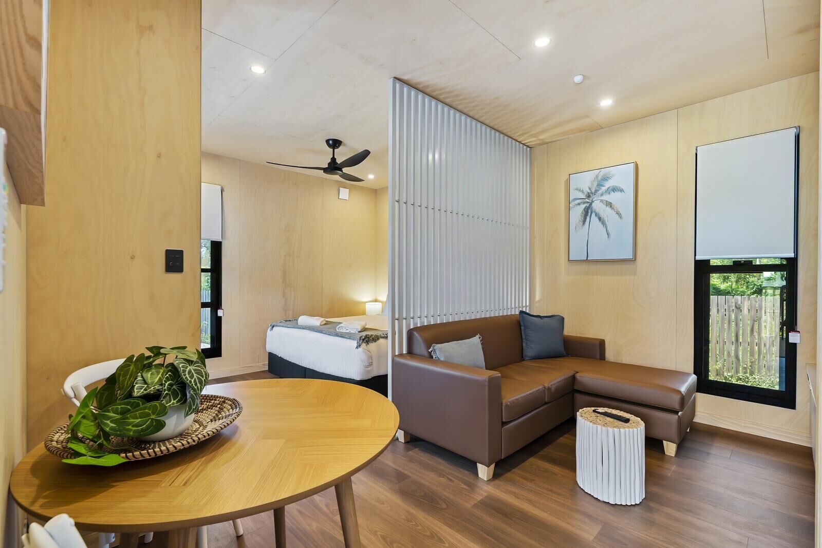 Una habitación de hotel moderna con cama, sofá, mesa de comedor y ventilador de techo.
