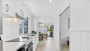 A modern kitchen with white cabinetry, stainless steel appliances, and a dining area with a table and chairs. - Ingenia Holidays Kinka Beach Yeppoon (Kinka Beach)