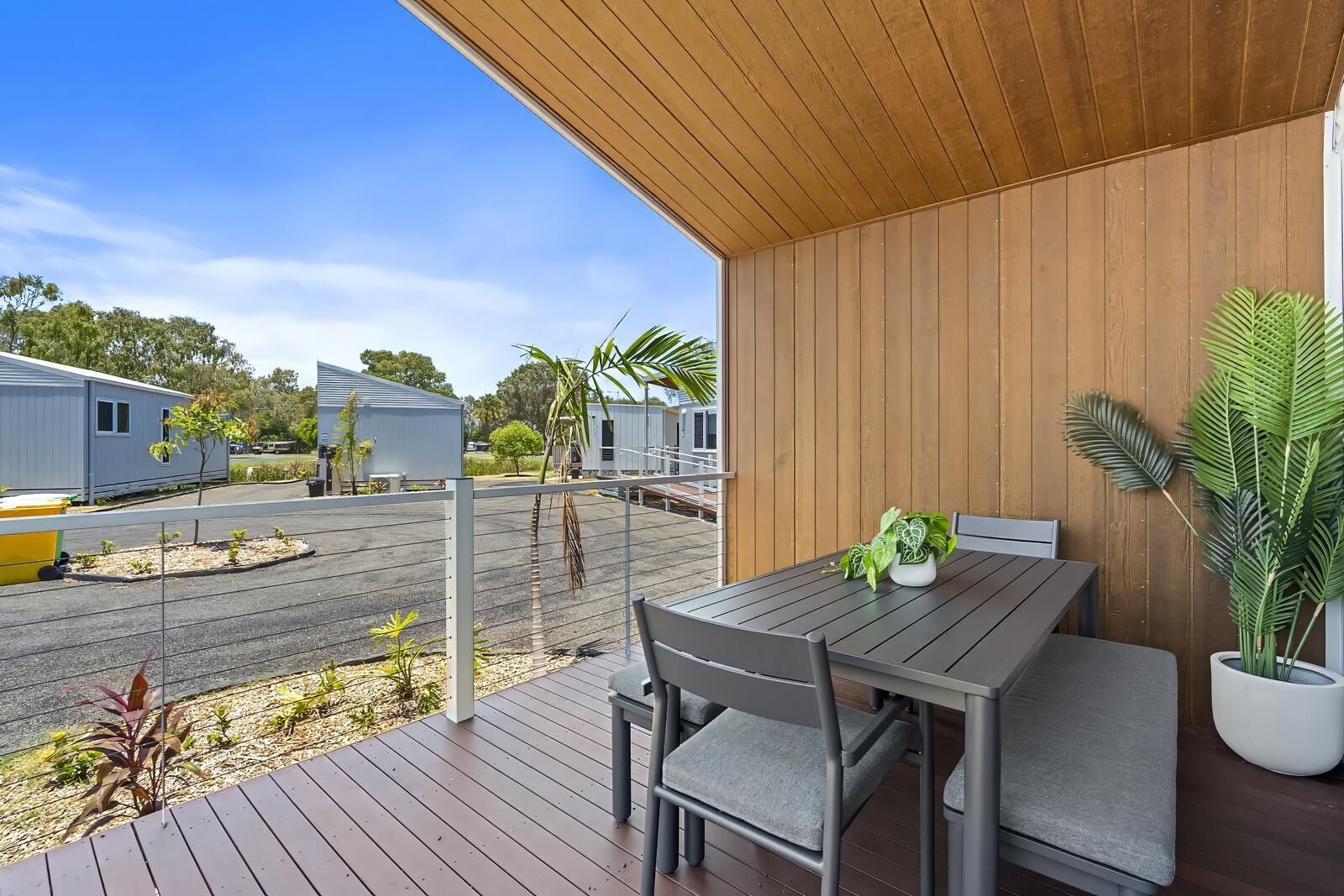 Une terrasse extérieure moderne, dotée d’une plateforme en bois, d’une table avec des chaises et de plantes en pot.