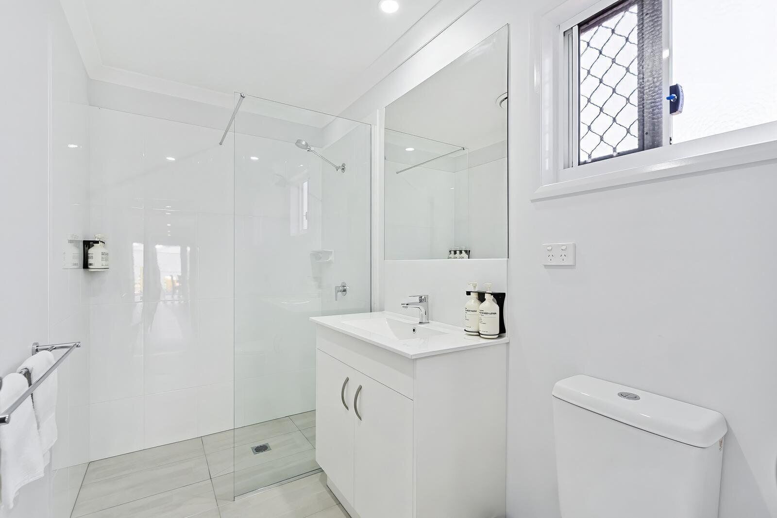 Un bagno moderno con box doccia in vetro, lavandino bianco con articoli da toilette e water.