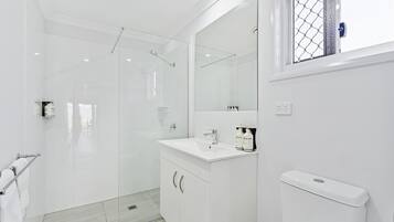 Un bagno moderno con box doccia in vetro, lavandino bianco con articoli da toilette e water.
