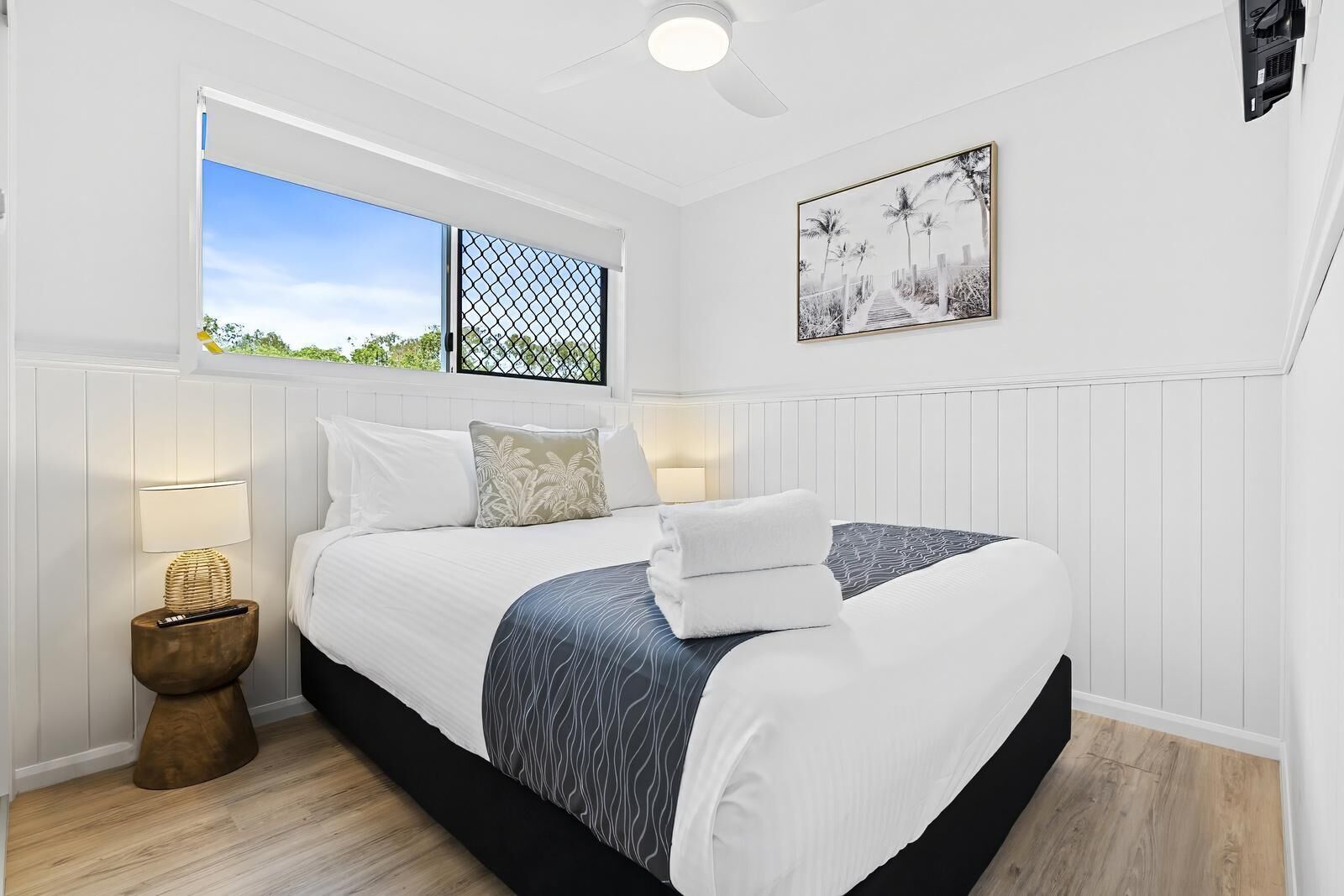 A bedroom with a bed, bedside lamps, a window with a view, and a ceiling fan.
