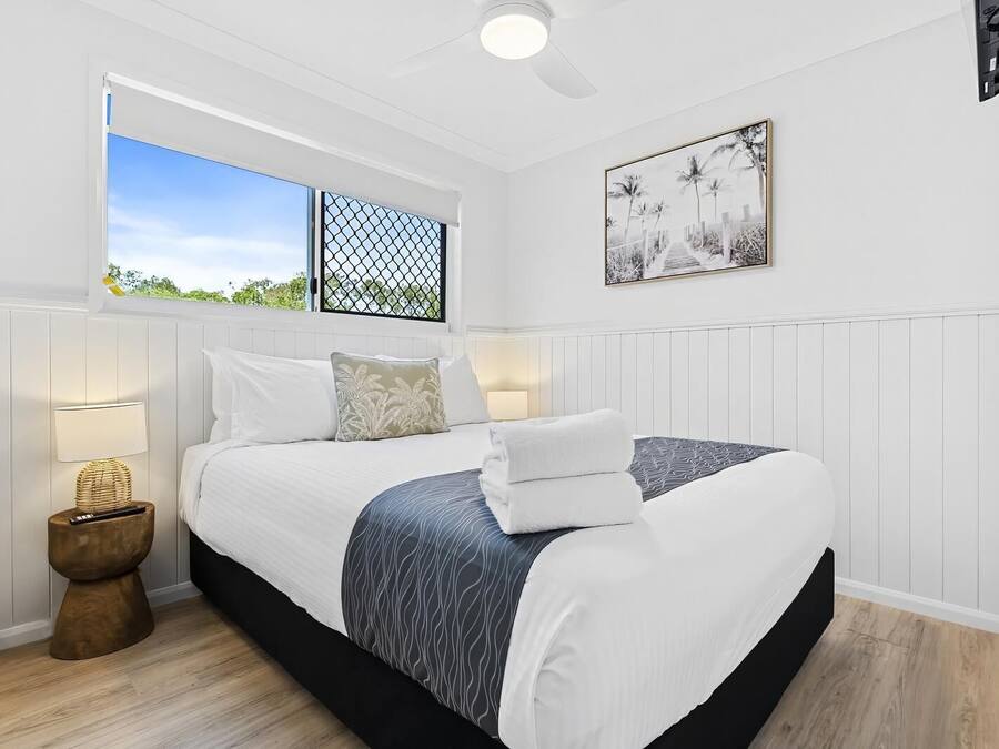 A bedroom with a bed, bedside lamps, a window with a view, and a ceiling fan.