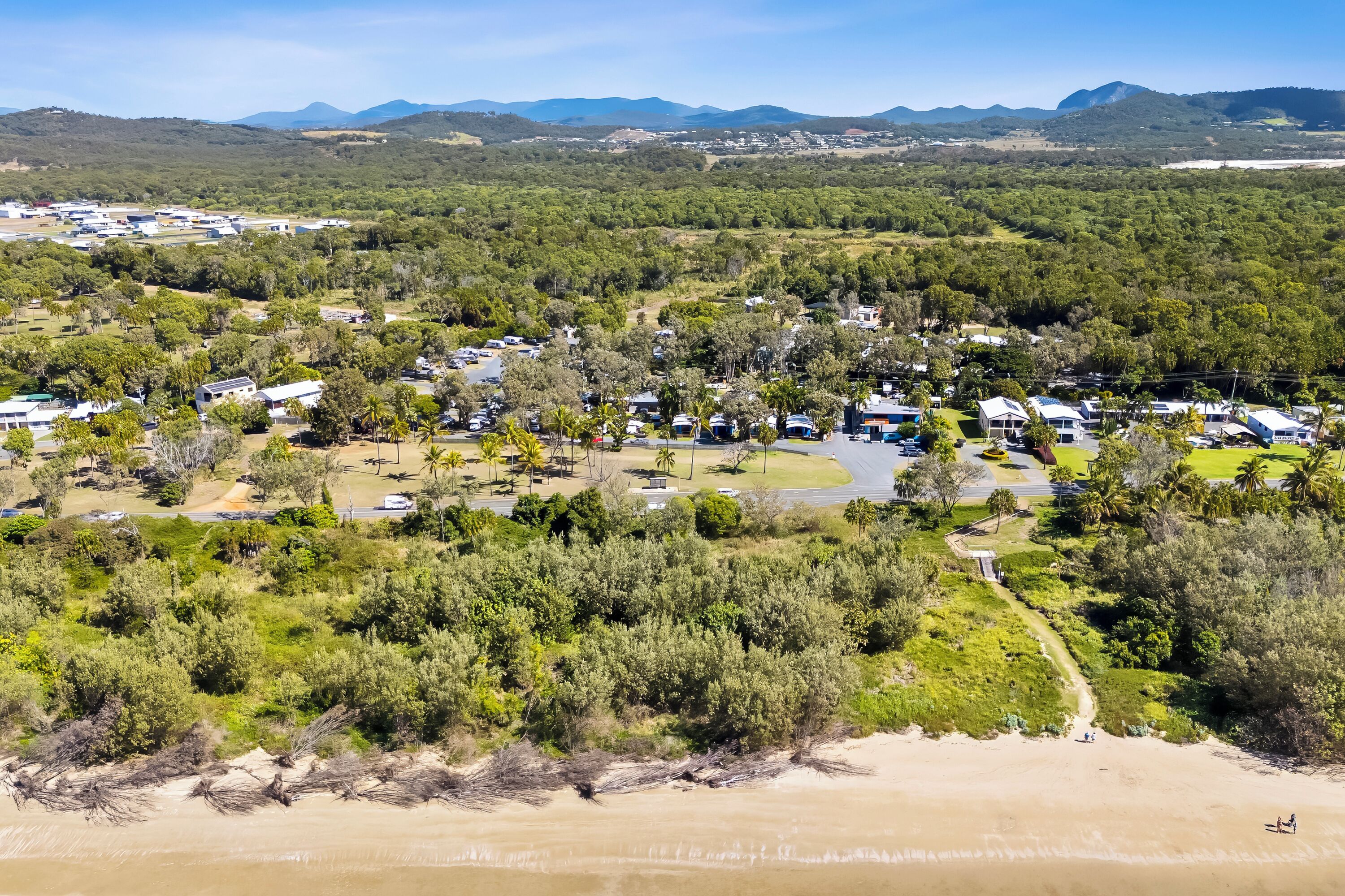 Vista aérea de un camping con vehículos recreativos, tiendas de campaña y cabañas, todo en medio de abundante vegetación y una playa.