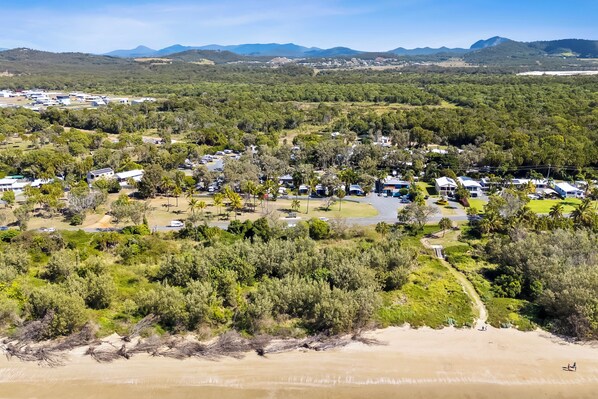 Vista aérea de un camping con vehículos recreativos, tiendas de campaña y cabañas, todo en medio de abundante vegetación y una playa.