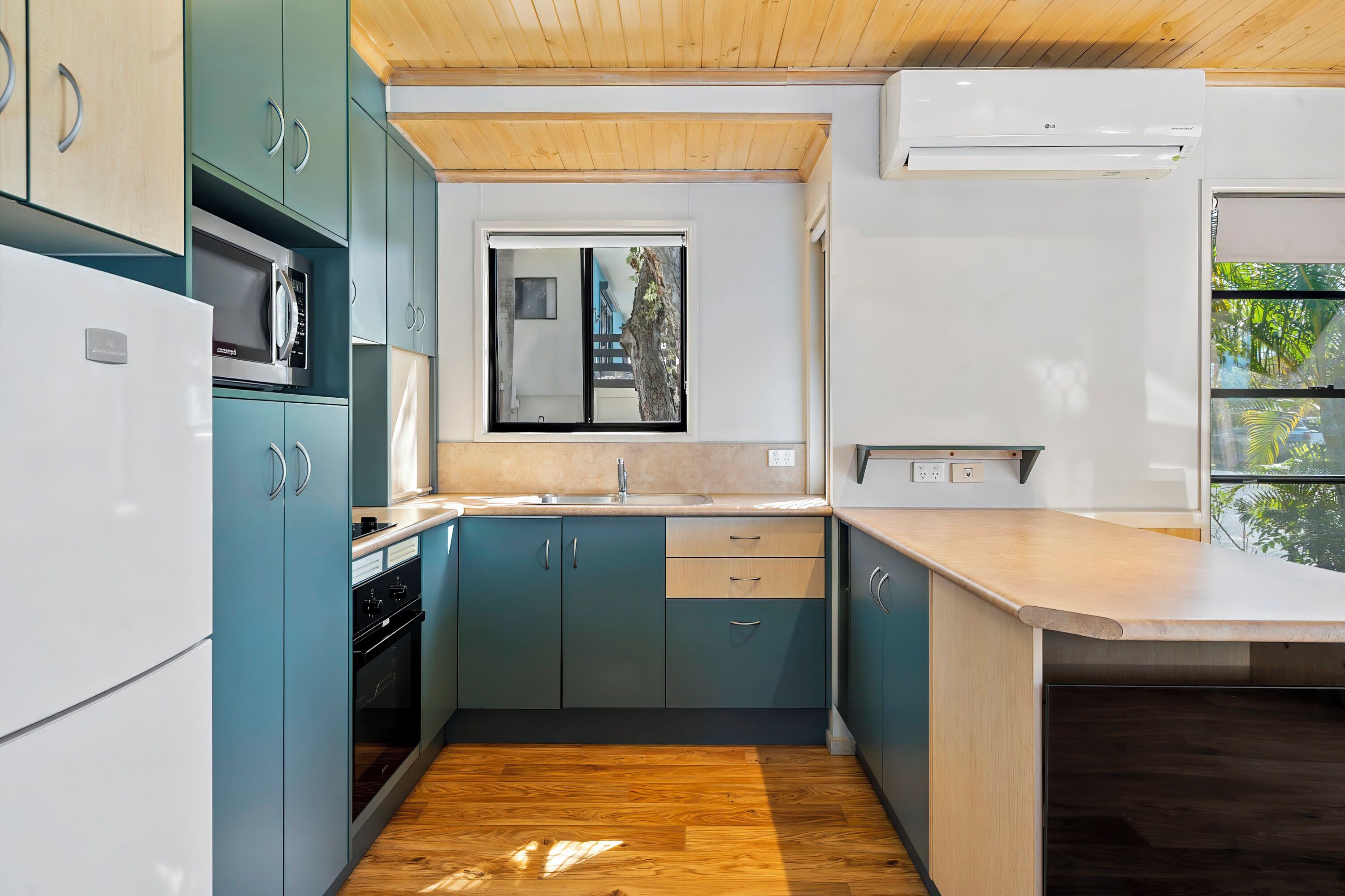 A modern kitchen with teal cabinets, a white refrigerator, and a wooden floor.