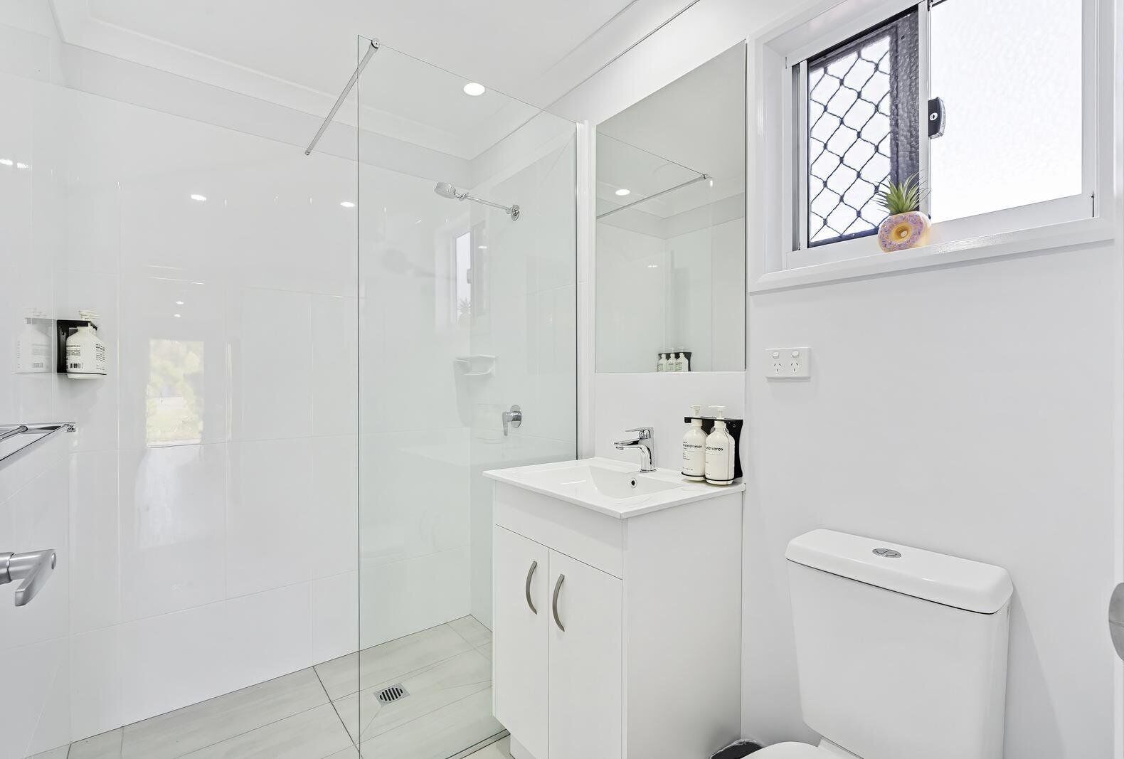 A modern bathroom with a glass shower enclosure, a white sink with a mirror above it, and a toilet.