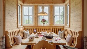 A wooden dining area with a bench and table, a hanging light fixture, and a window with a view of mountains. - Chalet Near Lake Grundlsee (Grundlsee)