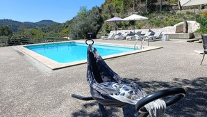 Area piscina con amaca, poltrone a sdraio e ombrelloni.