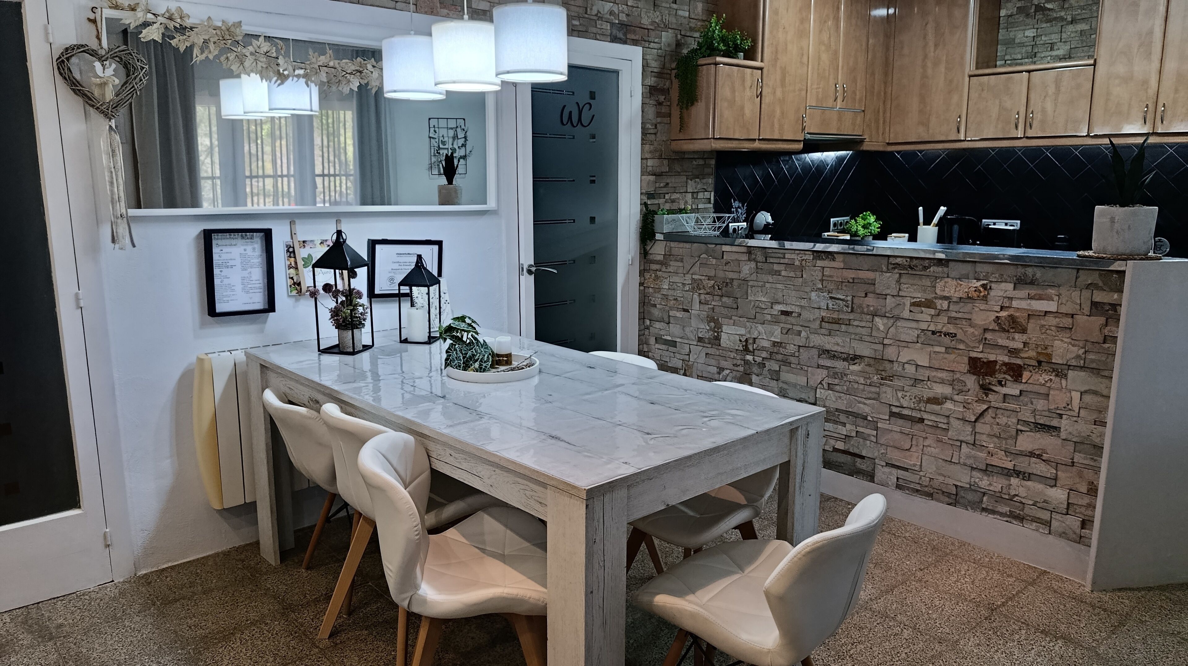 A dining area with a marble table, white chairs, and a kitchen with stone backsplash and wooden cabinets.