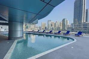 A rooftop pool with blue lounge chairs and a city skyline in the background.
