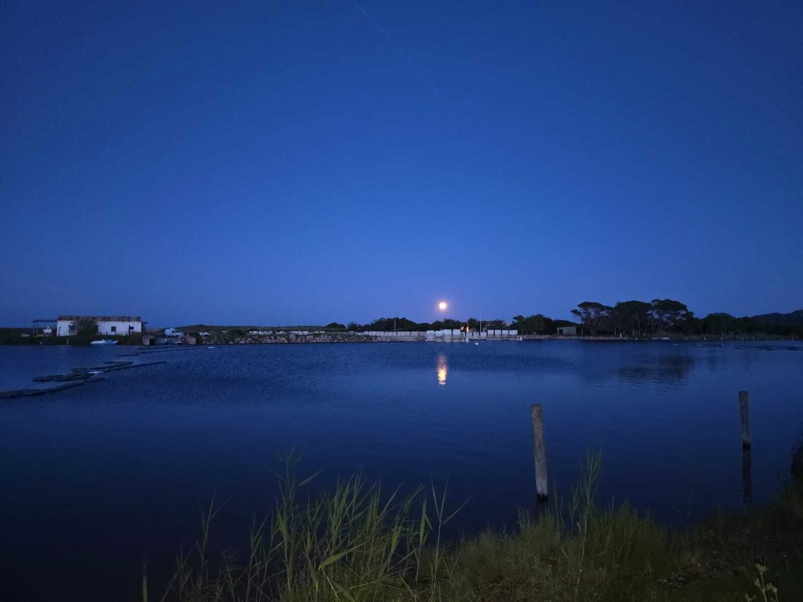 Um lago calmo ao entardecer, com uma pequena casa e um píer em primeiro plano.