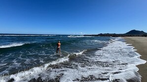 Una playa con olas, una persona y una montaña al fondo.