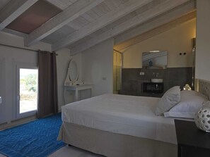 Una camera da letto con un letto, un comodino, uno specchio, un bagno con lavandino e doccia, e vista sull'esterno.