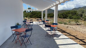 Patio esterno con tavoli e sedie pieghevoli, una pergola bianca e vista su un paesaggio montuoso.
