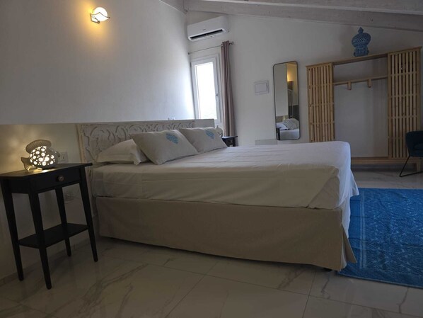 Quarto de hotel com cama, mesa de cabeceira, luminária, ar condicionado e um tapete azul.