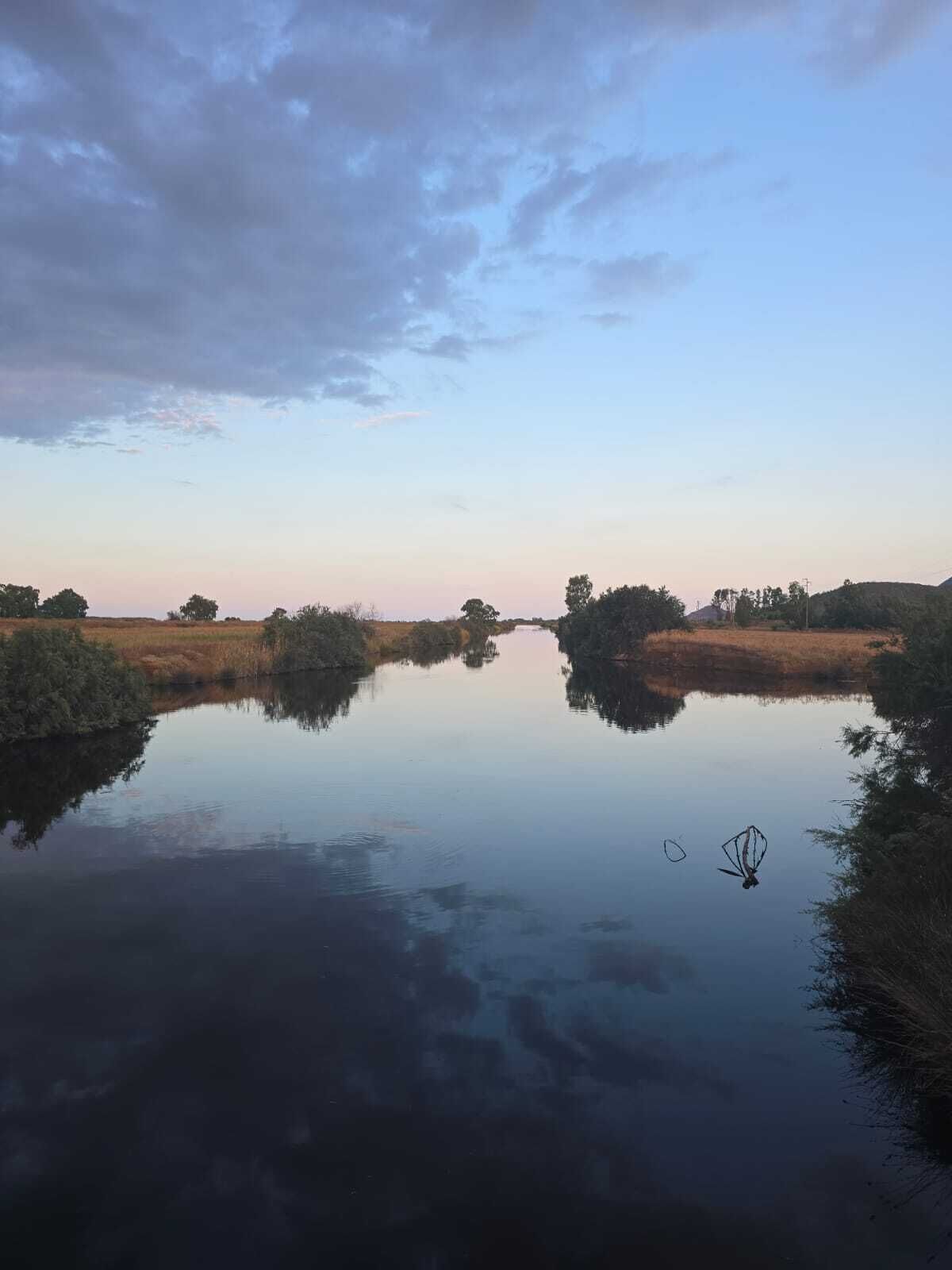 Un río tranquilo que refleja el cielo, rodeado de vegetación y árboles.