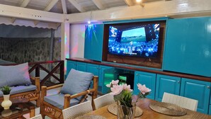 Ein gemütlicher Wohnbereich mit einer Couch, Sesseln, einem Fernseher und einem Tisch mit Blumen.