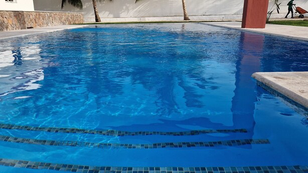 Ein klarer Pool mit blauen Fliesen und einer Steinwand.