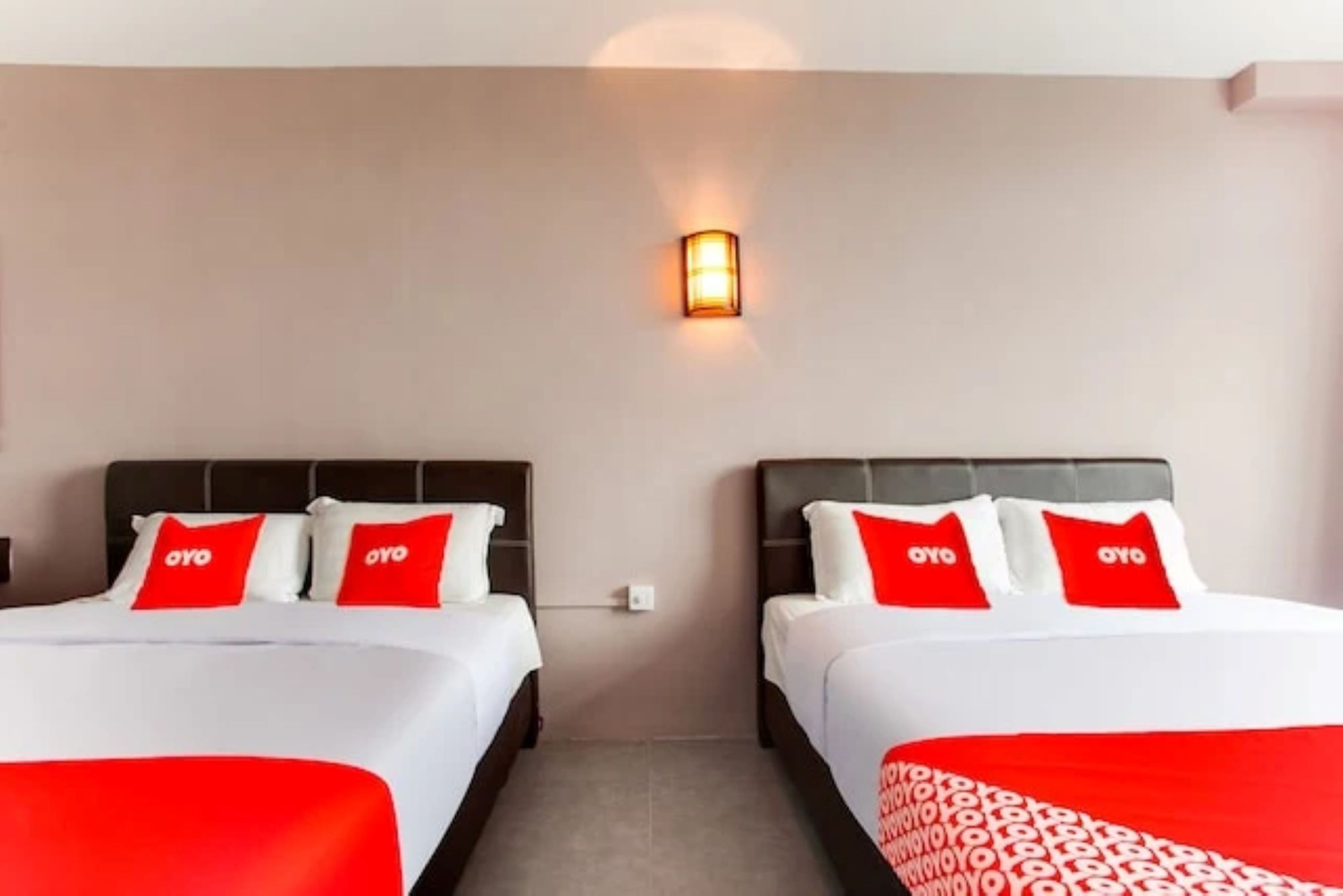 Ein Hotelzimmer mit zwei Betten, jeweils mit weißer Bettwäsche und roten Kissen, einer Wandleuchte und einer Wand in neutraler Farbe.