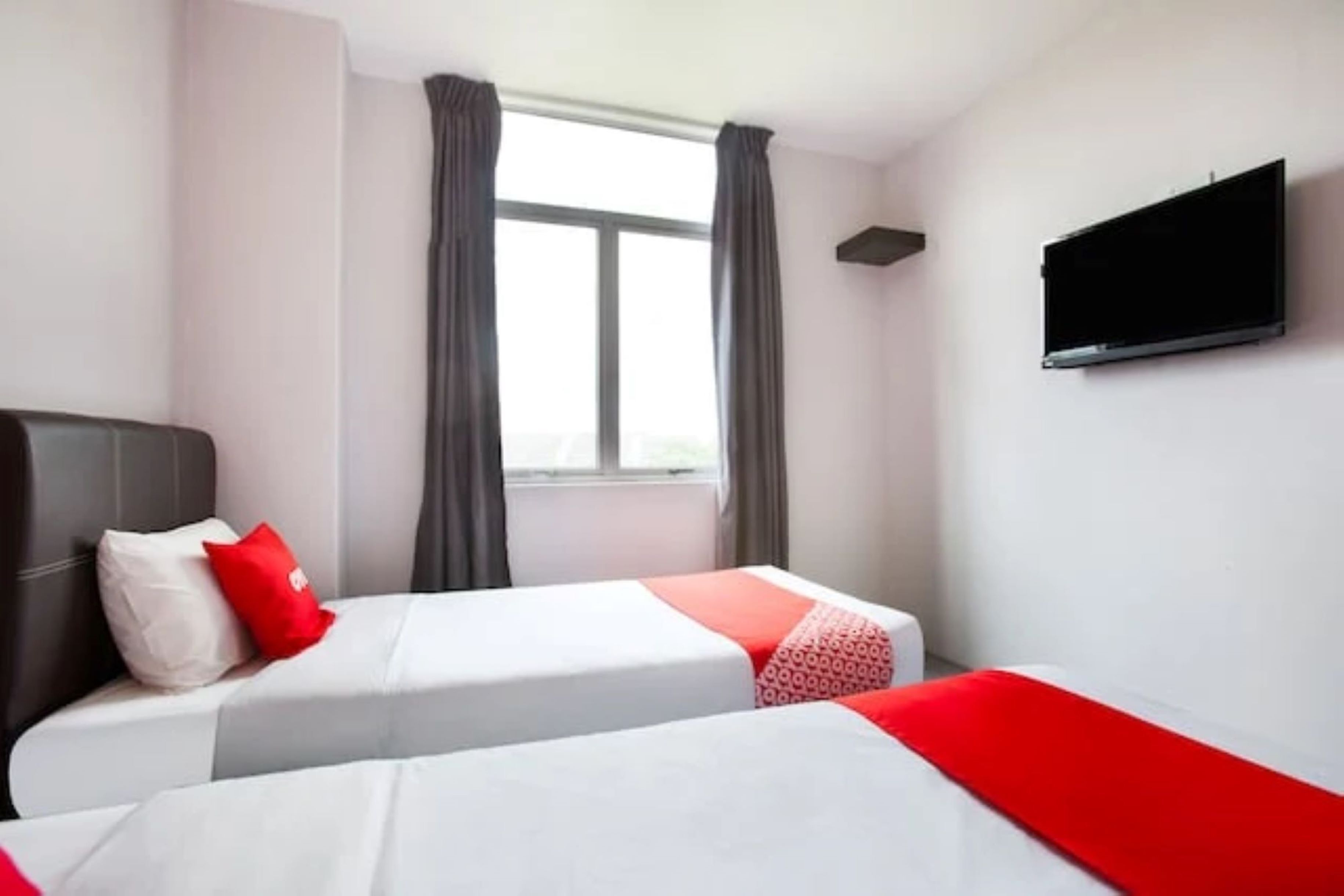 Hotellihuone, jossa on kaksi sänkyä, seinälle asennettu televisio ja ikkuna, jossa on verhot.