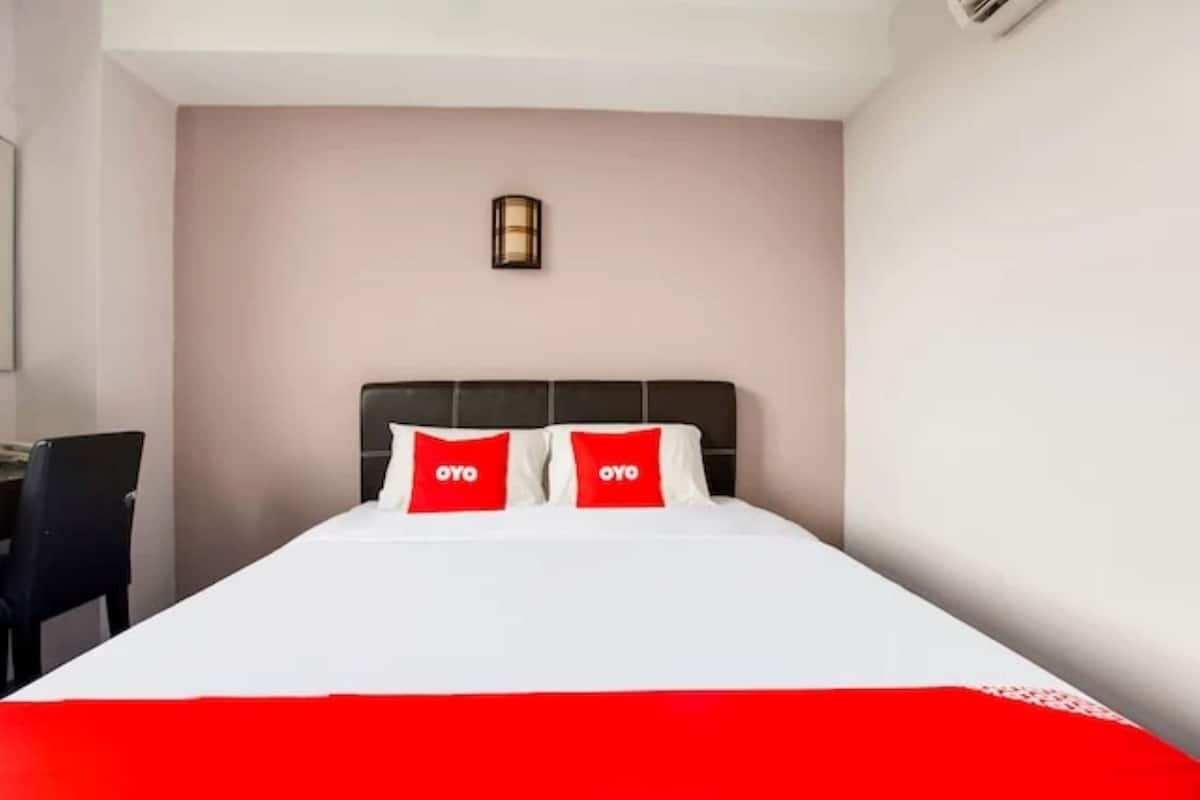 Una camera d'albergo con un letto, due cuscini con il marchio "OYO", un comodino, una scrivania e una sedia.