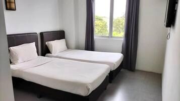 Habitación de hotel con dos camas individuales, ventana con cortinas y televisor de pantalla plana montado en la pared.