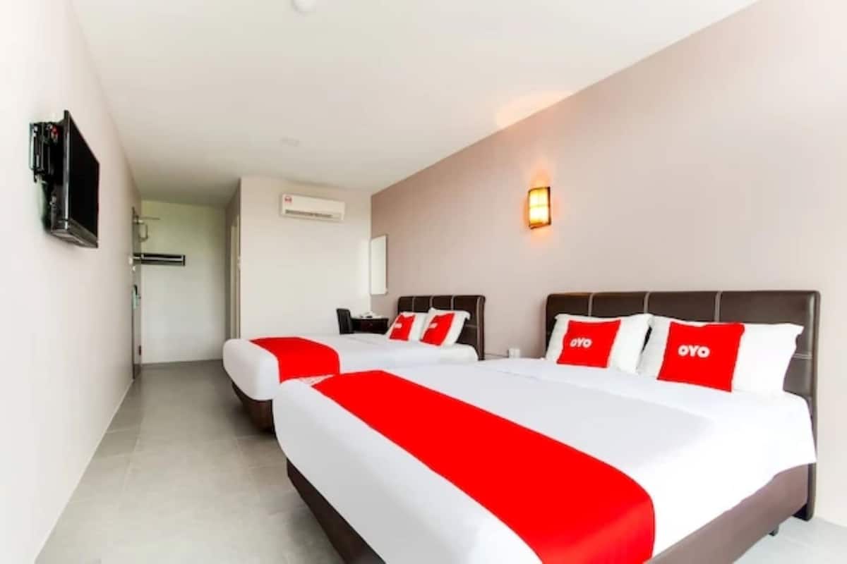 Una camera d'albergo con due letti, ciascuno con una coperta e dei cuscini rossi e bianchi. È presente una TV a muro e un lampadario fissato alla parete.