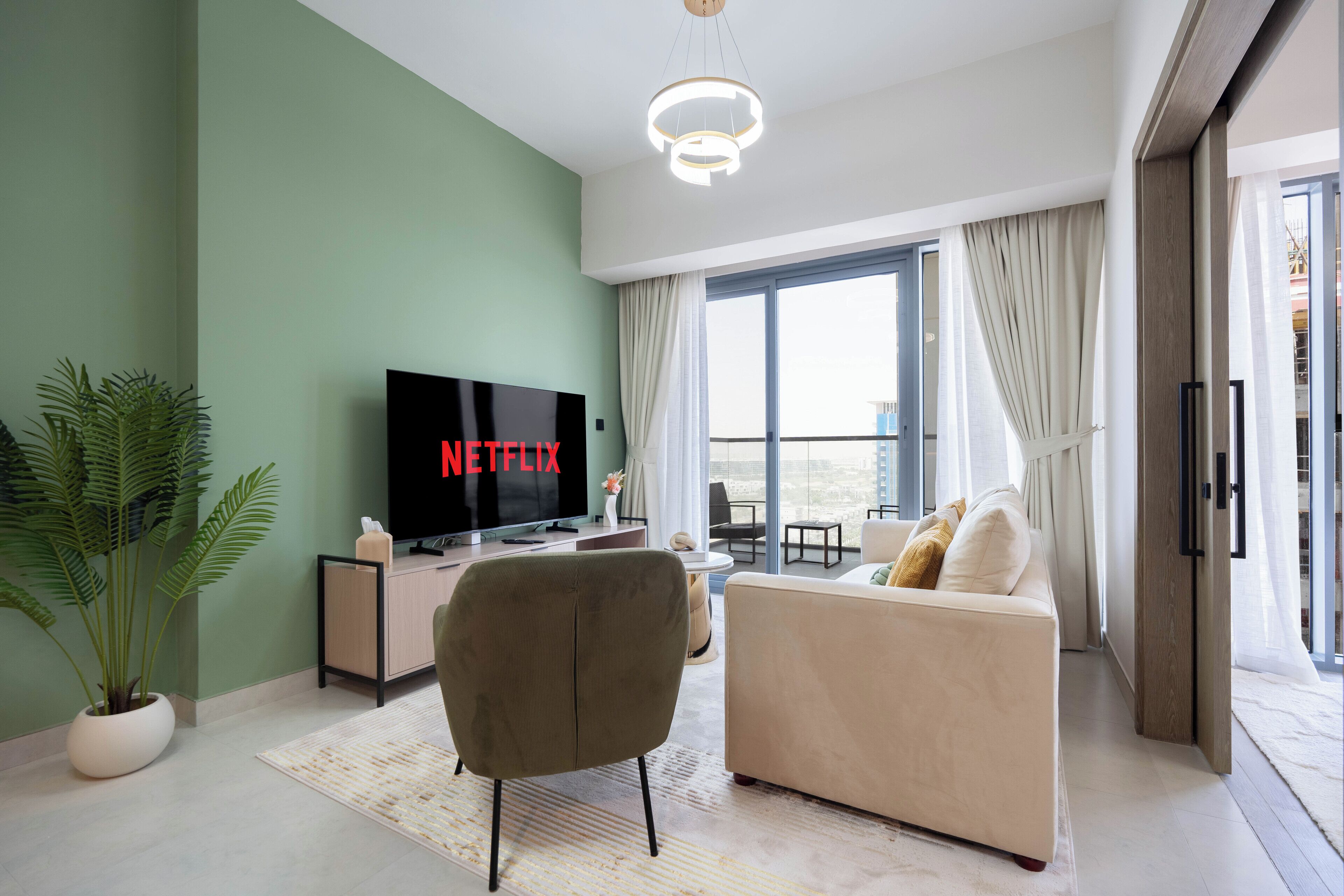 Ein modernes Wohnzimmer mit Fernseher, einer Couch, einem Couchtisch und einem großen Fenster mit Blick ins Freie.