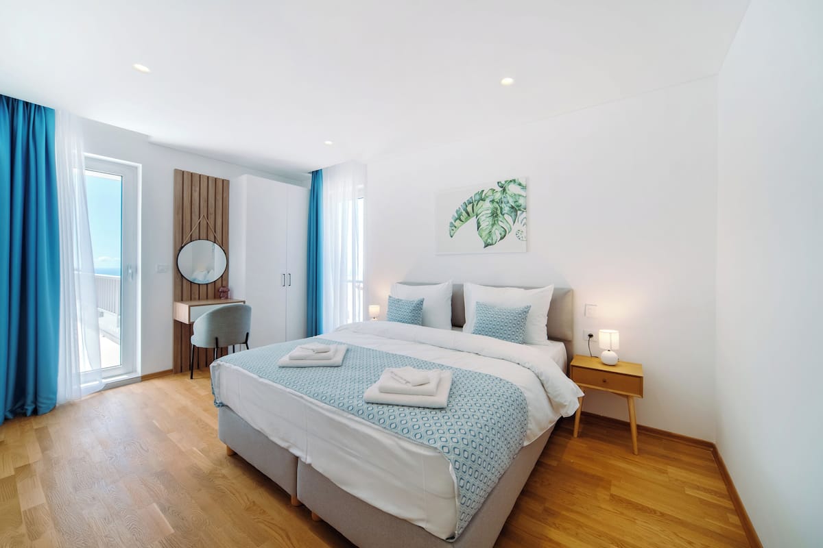A modern hotel room with a large bed, a desk, and a view through a glass door.