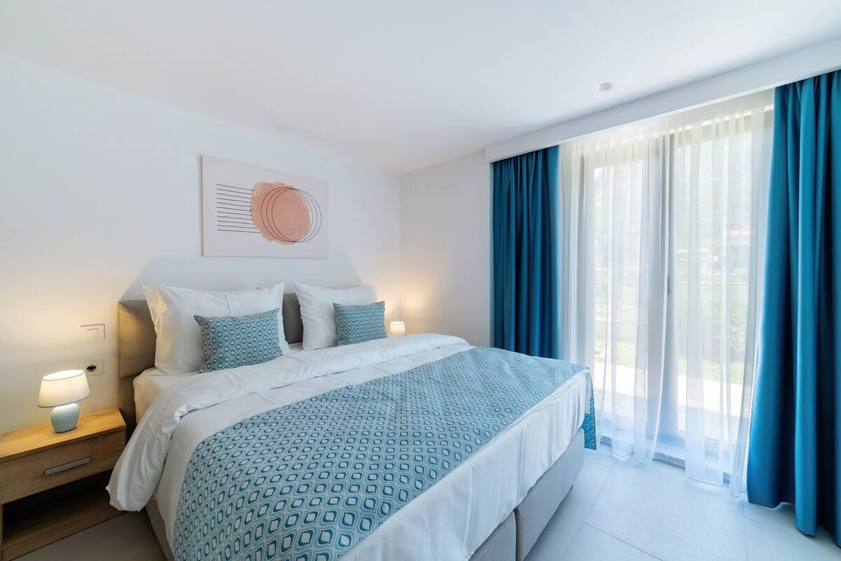 A hotel room with a large bed, a bedside table with a lamp, and a window with curtains.