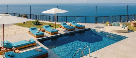 A poolside area with lounge chairs and a view of the ocean.