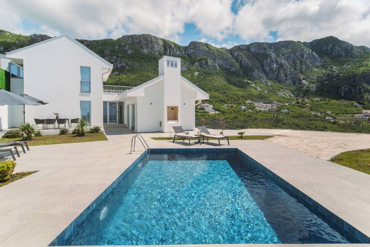 A modern house with a swimming pool, lounge chairs, and a mountain backdrop.