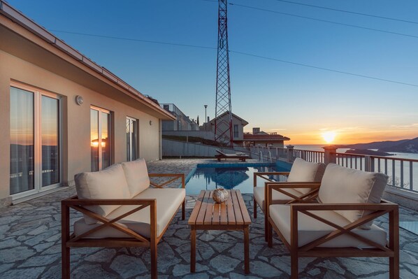 A rooftop terrace with a pool, seating area, and a view of the sunset over the sea. - Carsko Selo (Sveti Stefan)