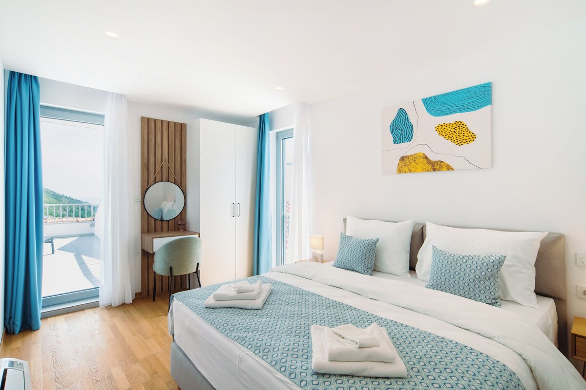 Une chambre d’hôtel avec un lit, un bureau, une chaise, un miroir rond et une fenêtre avec des rideaux.