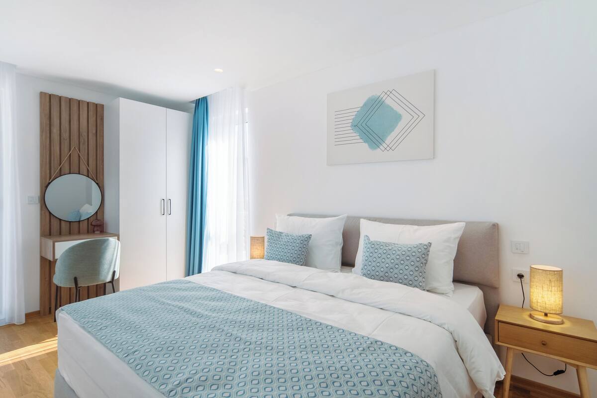 A bedroom with a bed, bedside table, lamp, and a wall-mounted mirror.