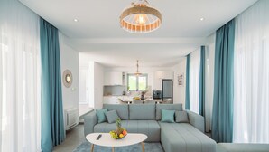 Una sala moderna con un sofá modular, una mesa de centro redonda y una cocina al fondo.