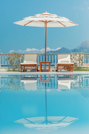 A clear blue pool with two lounge chairs and a wooden table under a large umbrella. - Carsko Selo (Sveti Stefan)