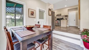 A dining area with a wooden table and chairs, a window with a view, and a kitchen in the background. - Stylish Urban Escape - Close to DTK and Expwy (Kitchener)