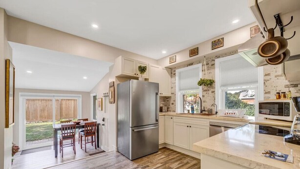 A kitchen with a stainless steel refrigerator, white cabinets, a microwave, and a window with a view of the outdoors. - Stylish Urban Escape - Close to DTK and Expwy (Kitchener)